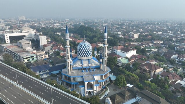Aerial view of Masjid Jami Al-Azhar Jakapermai with its distinctive blue dome and minarets surrounded by residential rooftops and a nearby highway in Bekasi Barat, West Java, Indonesia.
