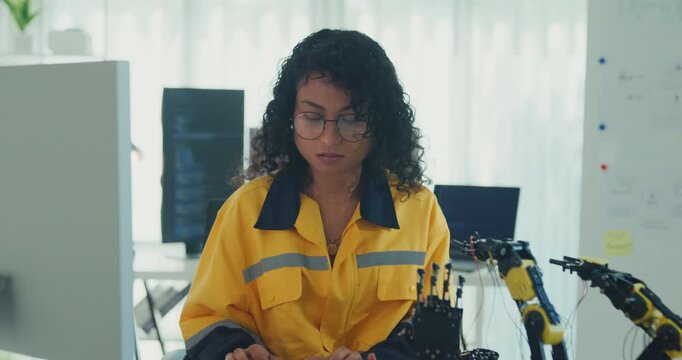 Young African American female robotics engineer coding AI software for robotic arm in laboratory. Embedded system, firmware testing, machine learning, industrial automation, future technology concept.
