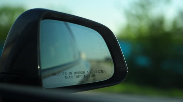 Closeup of vehicle side mirror during road travel, perspective while driving through a scenic landscape at sunset.