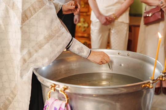 Orthodox priest blessing holy water in baptism font with cross oil brush