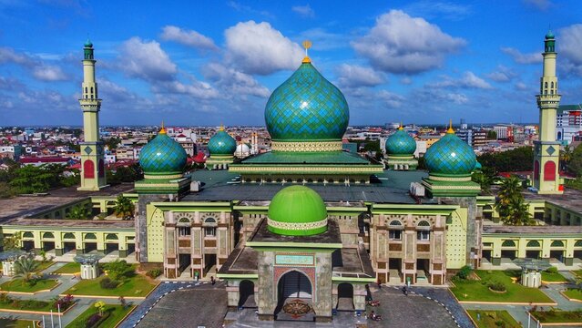 Aerial view of An-Nur Great Mosque with its distinctive green domes and minarets surrounded by gardens and the city skyline in Pekanbaru, Riau, Indonesia.