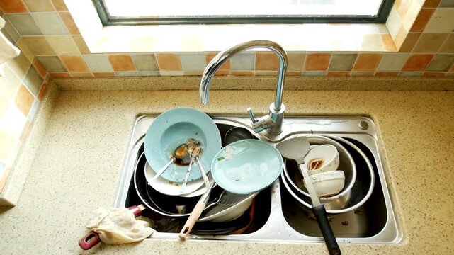 Dirty dishes and kitchen utensils piled up in a stainless steel sink
