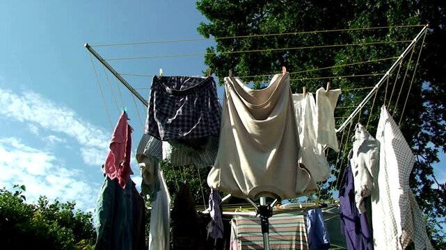 Laundry hanging on a rotary clothesline outdoors against a blue sky