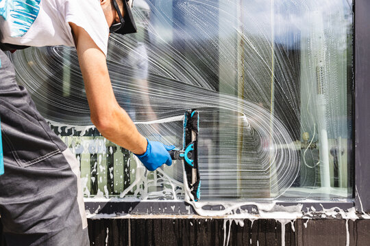 Professional window cleaner washing glass with squeegee and soapy water.