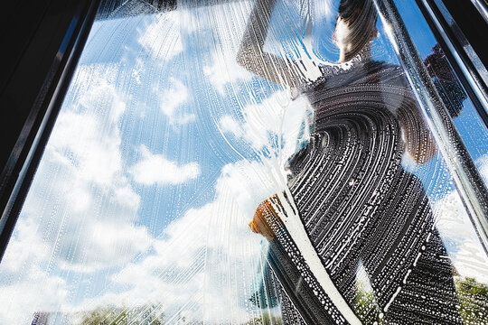 Professional worker cleaning a glass window with squeegee and soapy water.