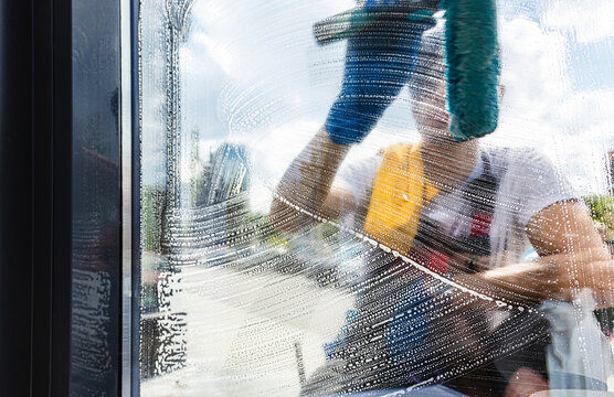 Professional window cleaner applying soapy suds to glass with a squeegee.