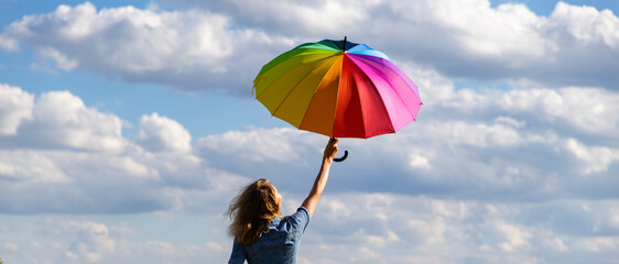 person holding rainbow umbrella against blue sky pride month © Melinda Nagy