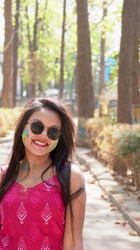 Beautiful smiling happy young Indian woman wearing colorful Gulal powder on her face and stylish sunglasses celebrating the outdoor spring festival of Holi and Dol Purnima or Dol Jatra festival.