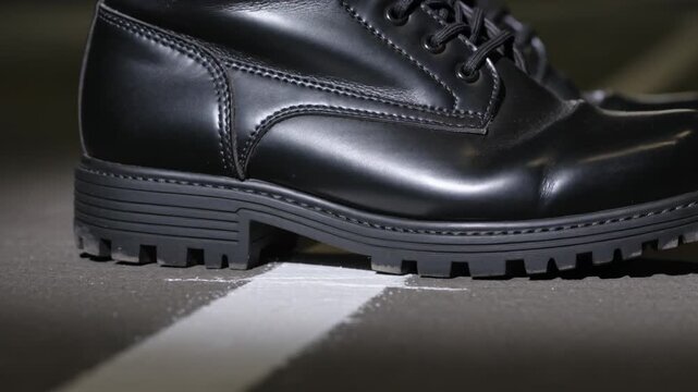 Stepping black leather laceup boot pushing heel onto white line on pavement, leaving paint chips