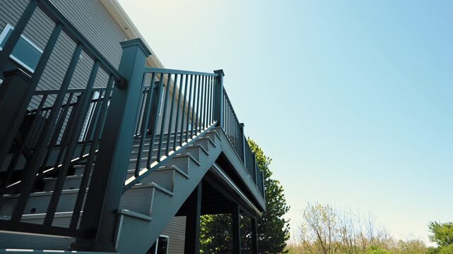 Modern elevated backyard deck attached to house featuring black metal railings, outdoor stairs. Move camera