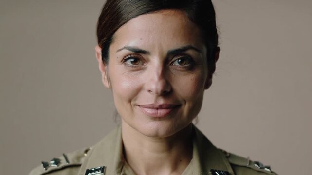 Recording uniformed woman softening mouth and smiling in studio for camera, showing khaki insignia