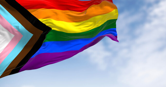Progress Pride Flag waving against cloudy blue sky