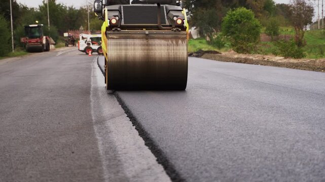 Road roller compacting fresh hot asphalt during road construction and paving works on a new highway