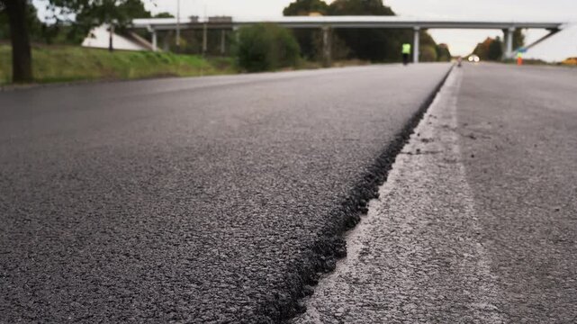 Freshly paved road with new asphalt and a white line marking showing a highway repair in progress during daytime construction