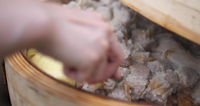Hand scooping fresh steamed pork shumai dumplings in bamboo steamer