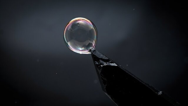 Magnified view of a clear soap bubble atop a black tool against dark background