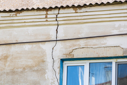 Severe vertical crack in stucco wall of old house above window, concept of building foundation failure, structural damage inspection, insurance claim and real estate defect assessment background