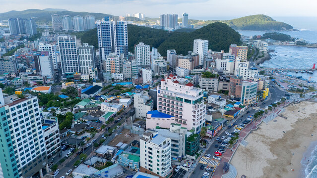Aerial view of the coastal district of Songjeong-dong featuring high-rise residential buildings, hotels, a sandy beach, and a harbor in Busan, Busan, South Korea.