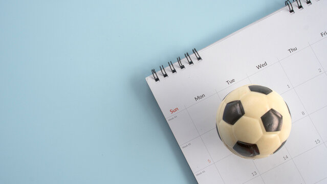 A small soccer ball placed on top of a monthly desk calendar page, representing sports scheduling, match day planning, or a tournament calendar.