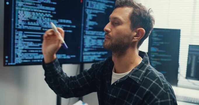Young Caucasian male programmer write creative plan on whiteboard and coding on computer in home office workspace. AI technology, cybersecurity network, agile strategy, business innovation concept.