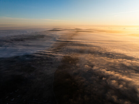 Aerial view of Lake Babite covered in thick morning fog during sunrise with golden light illuminating the clouds Marupes novads, Latvia.