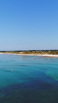 aerial view of a beach and ocean with surfers having fun on a bright summer day - vertical video for story and reel