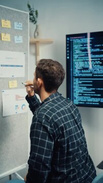 Vertical Screen : Young Caucasian male programmer write creative plan on whiteboard and coding on computer in home office. AI technology, cybersecurity network, agile strategy, business innovation.