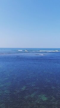 aerial view of a beach and ocean with surfers having fun on a bright summer day - vertical video for story and reel