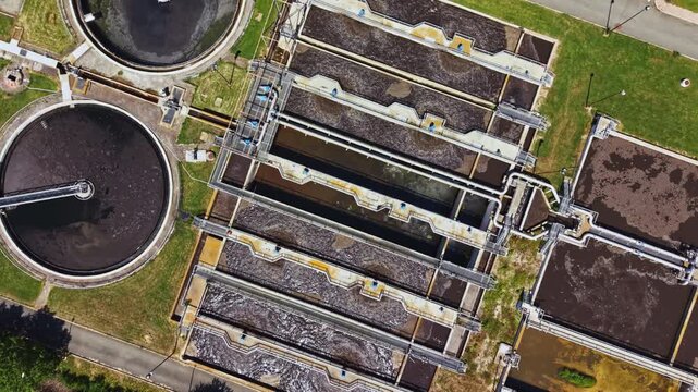 Topdown view sewage treatment basins operations with clarifiers and rectangular lanes, inspectors monitoring sludge levels, compliance sampling pathways, road
