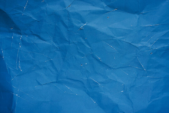 Distressed blue paper texture background with crumpled surface and white scratches 