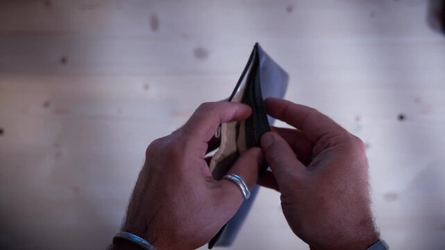 Poverty and financial struggle represented by hands holding an empty black leather wallet. Moody high-contrast visual style in a close-up eye-level view during a stressful moment.