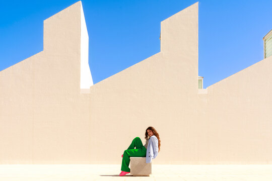 Person Sits on a Box in Front of a Blank Wall on a Sunny Day