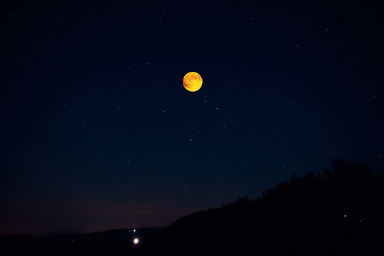 Full Moon on a twilight sky with countryside silhouettes.
