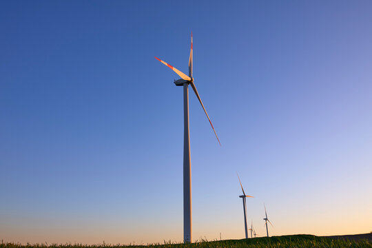 Wind turbines at sunset in green field &ndash; renewable energy, clean power, sustainable future.