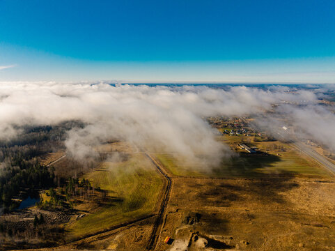 Aerial view of low-hanging clouds drifting over rural fields and the A8 highway in Olaine parish, Olaine Municipality, Latvia.