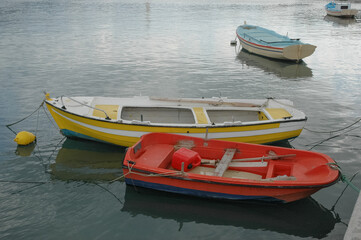 Small traditional wooden fishing and rowing boats in red, yellow, and blue colors moored on calm water in a Greek harbor © nahhan