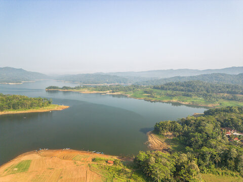 Aerial view of Wadaslintang Reservoir surrounded by lush green hills and forests with agricultural fields along the shoreline in Wadaslintang, Central Java, Indonesia.