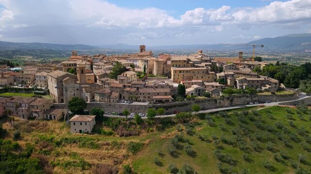 Montefalco Umbria Italy 4k drone backward pullback reveal of medieval borgo town. Aerial wide panoramic view of historic hilltop walled village green fields vineyards and olive trees b-roll
