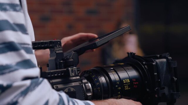 Camera operator adjusting the recording settings. Unrecognizable person sitting on a chair in the background. Selective focus