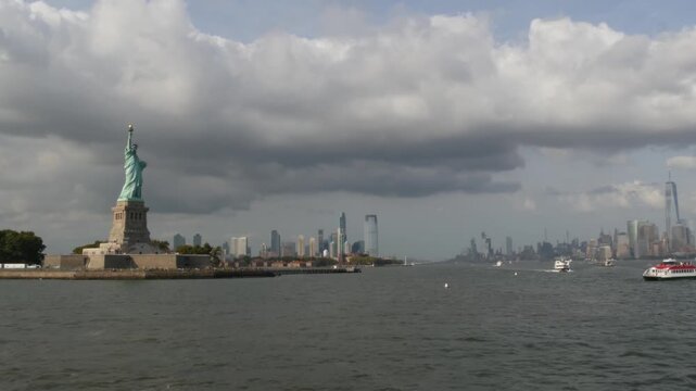 Statue of Liberty on Liberty Island, New York, United States. Cooper monument, symbol of democracy and patriotism near Manhattan, NYC USA. View from river ferry boat, tourist cruise. Cityscape skyline