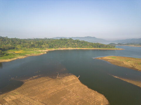 Aerial view of Wadaslintang Reservoir surrounded by lush green hills, agricultural fields, and calm water under a clear blue sky in Wadaslintang, Central Java, Indonesia.