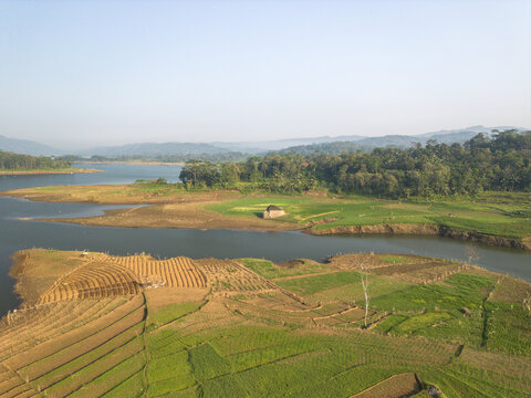 Aerial view of Wadaslintang Reservoir surrounded by lush green agricultural fields, terraced farms, and dense forests in Wadaslintang, Central Java, Indonesia.