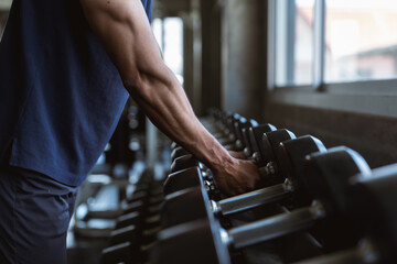 Naklejka premium Close up of strong sportsman arm holding heavy dumbbell iron piece. Active male exercising power strength routine at indoor sport club fitness