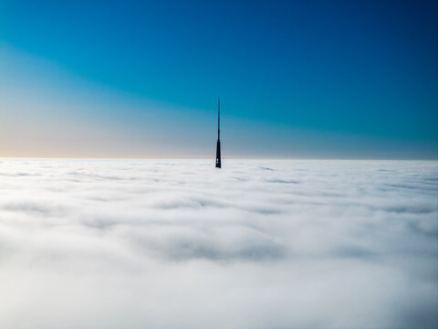 Aerial view of Riga Radio and TV Tower rising above a thick layer of clouds under a clear blue sky in Riga, Latvia.