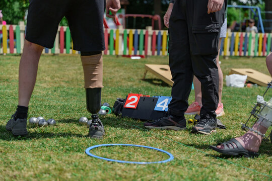 People with prosthetic legs play petanque on a green grass field. Adaptive sports game, veteran rehabilitation, outdoor leisure in Ukraine.