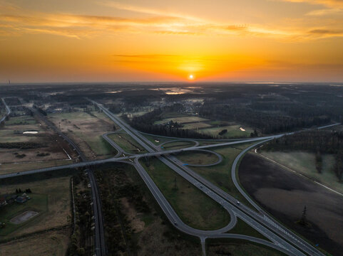 Aerial view of the A5 and A8 highway interchange at sunset, featuring multi-level roads, surrounding fields, and golden light in Olaine parish, Olaine Municipality, Latvia.