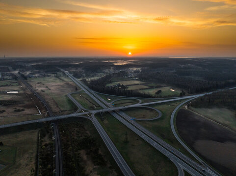 Aerial view of the A5 and A8 highway interchange at sunset with surrounding fields and forests in Olaine parish, Olaine Municipality, Latvia.