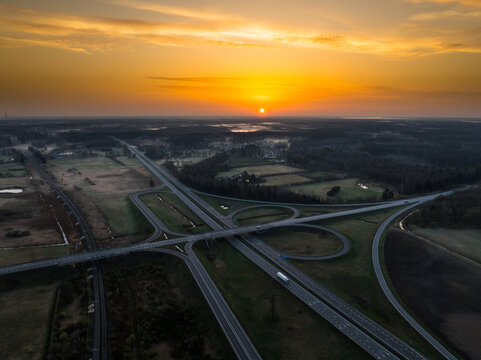 Aerial view of the A5 and A8 highway interchange at sunset, with golden light reflecting on the asphalt and surrounding rural landscape in Olaine Parish, Olaine Municipality, Latvia.