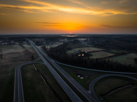 Aerial view of the highway interchange between the A5 and A8 roads at sunrise, with surrounding fields and forests in Olaine parish, Olaine Municipality, Latvia.