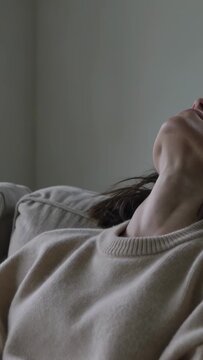 Vertical video: Furrowed brow pushing woman in beige knit sweater breathing to calm on sofa cushion